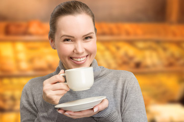 happy young woman with a cup of fresh coffee in her hand and bakery in background 