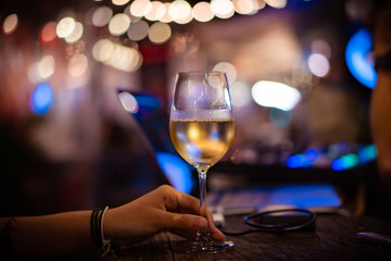 Glass of White Wine in Hand with Blurred Bokeh Light Background. White Wine Glass Outdoor.