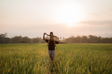 daughter piggybacking on father's shoulders when playing together in the rice field