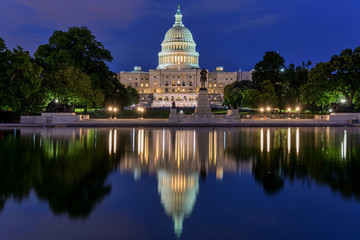 The Capitol in Reflecting Pool - A dusk view of west side of U.S. Capitol Building, with a crowd gathering around a concert at front, Washington, D.C., USA. No recognizable trademark or person.