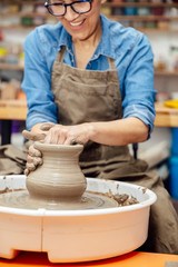 Fototapeta na wymiar Senior female potter working on pottery wheel while sitting in her workshop