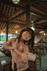 Asian little girl greets in traditional way with both hands, wearing kebaya traditional clothes from indonesia