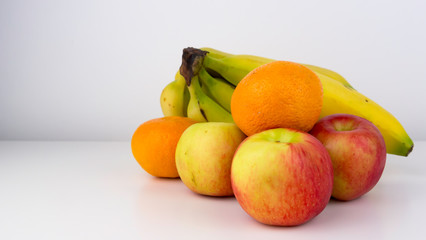 Collection of healthy fruit including Jazz apples, oranges and a bunch of ripe bananas featured on a white studio background.