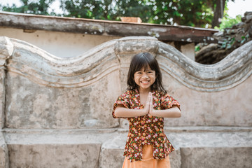 Happy little girl greeting in traditional way from indonesia with both hands gesture