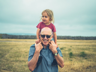 Little toddler riding on grandfather's shoulders in nature