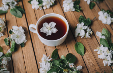 White cup of tea with petals of an apple tree on a wooden background, close-up.
