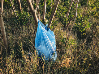Big plastic bag with trash at tree in park or forest. Plastic pollution. Garbage on grass after people holiday. Rubbish disaster. Ban single use. Zero waste