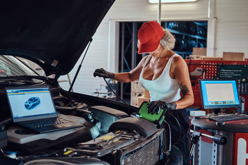 Manly strong woman is fixing car's engine with computer help at auto service.