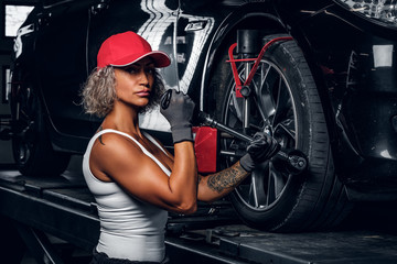 Fototapeta na wymiar Blond strong woman is doing man's job, fixing car's wheel with wrench at auto service.
