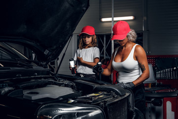Professional mechanic woman and her little helper are making great team, working on car's engine.