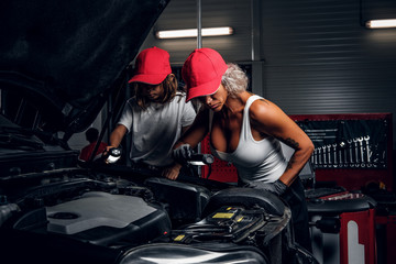 Fototapeta na wymiar Professional mechanic woman and her little helper are making great team, working on car's engine.
