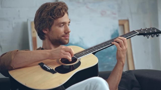 young man playing acoustic guitar on sofa