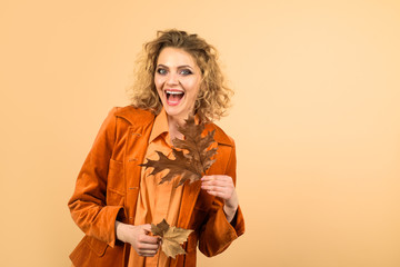 Autumn beauty. Perfect woman fashion model with fall leaves. Fashionable woman in orange jacket with yellow oak leaves. Fashion autumn woman portrait. Fresh skin. Healthy smile. Girl with autumn leaf.