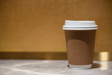 Brown paper coffee cup set on marble floor, on a golden background.