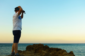 man looks through a telescope at the sea