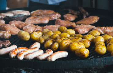 Cooking fast food on a huge grill at the fair. Different sausages and potatoes are grilled