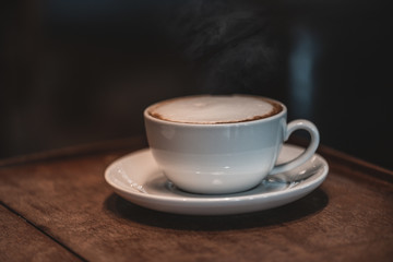 Hot coffee, cappuccino In a white cup with art foam. Near the window on the wooden table at the coffee shop