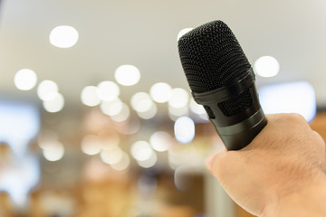 Close Up man's hand holding a microphone in the meeting room, blurred bokeh background