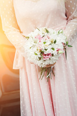 The bride in a pink dress on the wedding day holds a bouquet in her hands. Close-up. Toned photo.