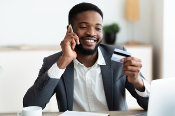 African worker holding credit card and talking on mobile phone