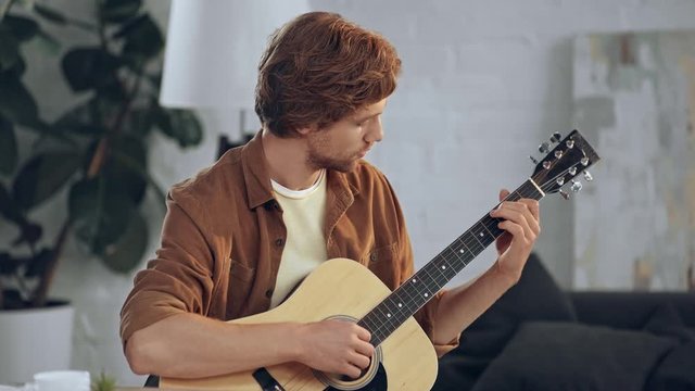young concentrated man playing acoustic guitar at home