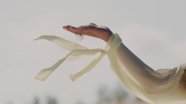 Woman on sand dune in fornt of blue sky pouring sand from hands and enjoying nature. Slow motion close up