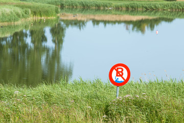 Warning sign prohibiting swimming over lake background.