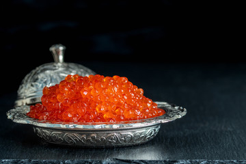 Red caviar in silver bowl on black background