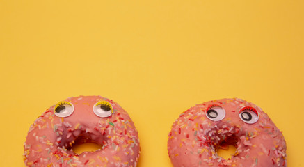 Two glazed pink donuts isolated with funny faces.