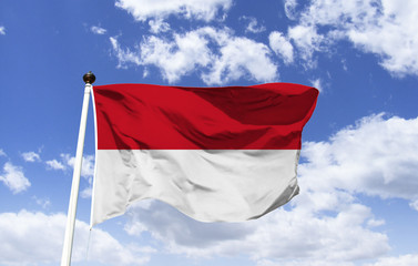Fototapeta na wymiar Monaco flag mockup in the blue sky. Highest symbol of the official representation of the country, with two horizontal fields in red and white, are heraldic colors that represent the house of Grimaldi.