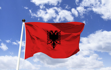 Albania flag mockup fluttering under blue sky. It is red with a double-headed black eagle, derived...
