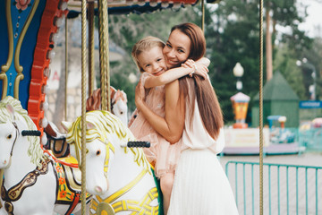 a little girl with her mother riding in the Park on a toy horse on the carousel. Entertainment industry concept, family day, children's parks, playgrounds © aaalll3110