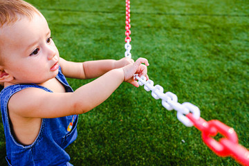 Baby playing with a chains in a park on the grass.