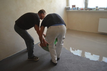 Mężczyźni wylewający masę wylewki samopoziomującej na posadzkę © Ewa