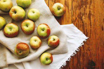 Ripe rustic apples on wooden background with beige and white linen cloth.