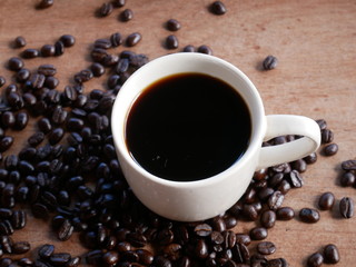 cup of coffee with beans on wooden background