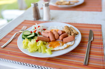 Plate with fried eggs, sausages, onions, cucumber, paprika and toasted sticks with sesame