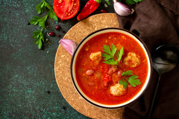 Tomato soup with meatballs and chili peppers on a dark stone or slate table. Top view flat lay. Free space for your text.