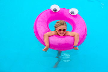 Adorable smiling girl playing with inflatable pink ring in swimming pool on summer vacation