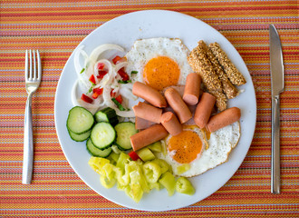 Plate with fried eggs, sausages, onions, cucumber, paprika and toasted sticks with sesame