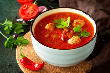 Tomato soup with meatballs and chili peppers on a dark stone or slate table.