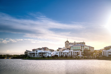  Wide panoramic view of Emerald Lakes residences across the lake, on a blue sky background during a beautiful sunset. Gold Coast, Australia.