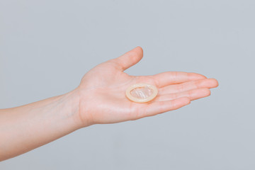 The condom lies on the female hand, close-up on gray background