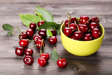 Sweet cherries in bowl with green leafs on wooden table