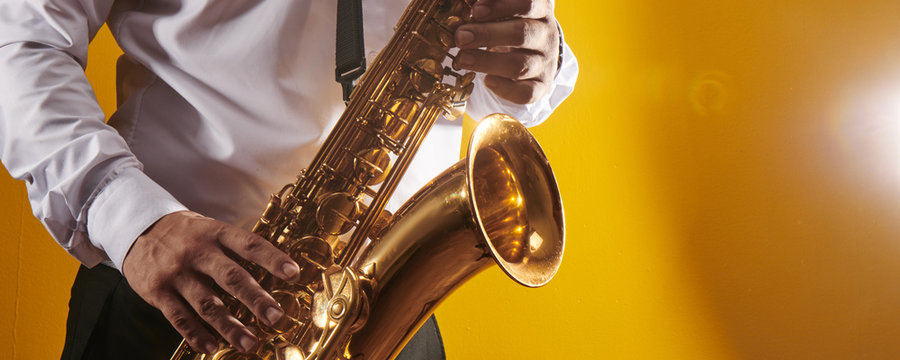 Professional musician saxophonist man in  white shirt plays jazz music on saxophone, yellow background in a photo studio, side view