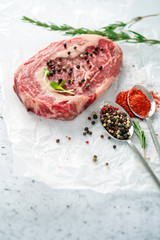 Raw marbled beef steak ribeye with spices, salt and pepper on white Kraft paper. The concept of organic fresh meat