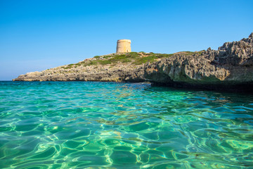 View on the beach Calo Roig with crystal water and the Defense Tower Alcaufar on Menorca.