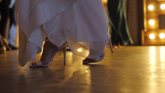 A bride dancing on the dance floor at a wedding reception in wedding dress slow motion shot of shoes on the dance floor backlit