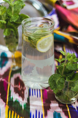 homemade lemonade in a jug with lime, mint and lemon on a colored background.