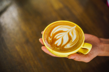 women hands holding cup of coffee latte art on old dark wood table. Top view.